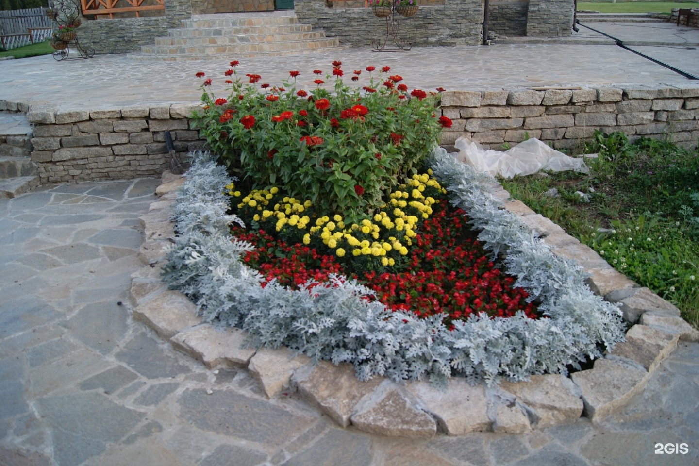 Круглая клумба с цветами, обложенная крупным камнем